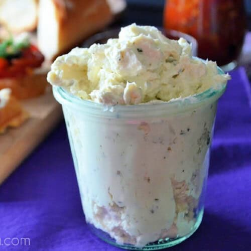 Glass jar with cream cheese dip on a purple cloth.