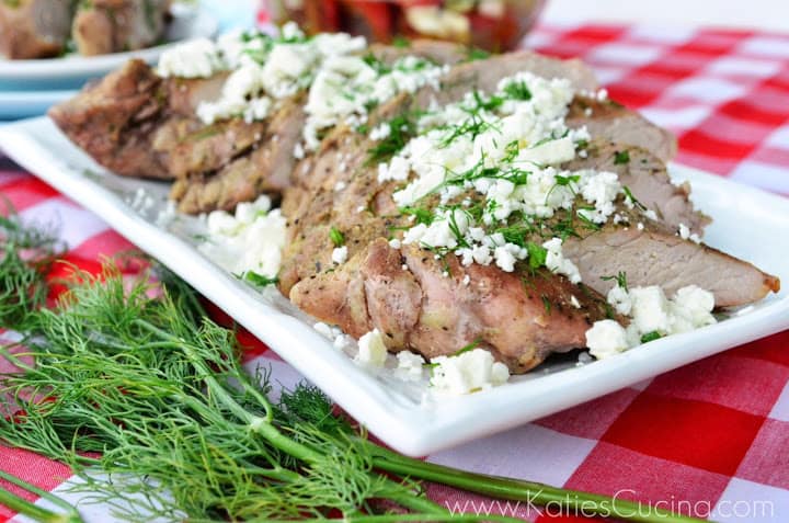 Plated grilled pork tenderloin topped with feta cheese and dill on picnic tablecloth.