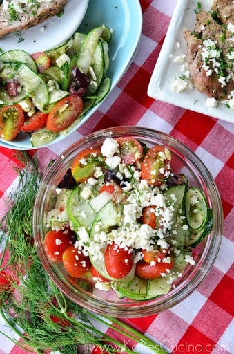 Top view greek cucumber, tomato, and feta salad artistically placed near dill on tablecloth.