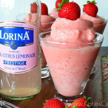 4 pink blended drinks topped with strawberries next to Lorina Pink Citrus Lemonade bottle.