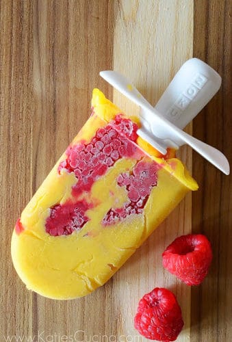 Orange colored homemade popsicle with raspberries in it on a board.