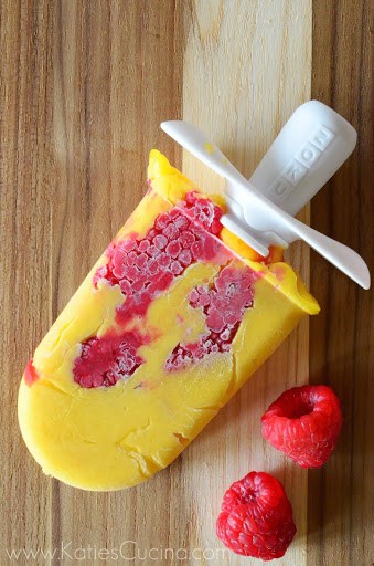 Orange colored homemade popsicle with raspberries in it on a board.