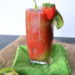 A single glass of strawberry kiwi juice over ice on a green cloth.