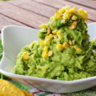 Guacamole in a bowl topped with grilled corn decoratively placed by cilantro.
