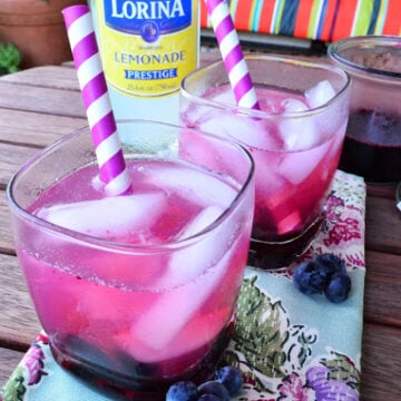 two glasses filled with pink beverage, ice, and two paper straws artfully placed next to blueberries.