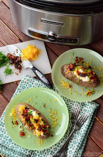 Top view of loaded baked potatoes on green plates with the slow cooker at the top of the photo.