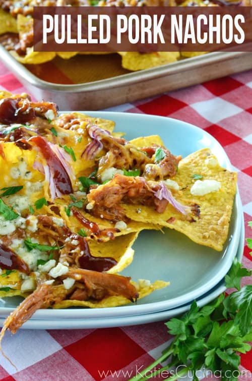 Two blue square plates stacked with nachos topped with pork, cheese, and red onions. 