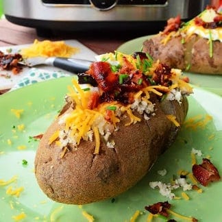 close up of a baked potato filled with cheese, bacon, and green onions.