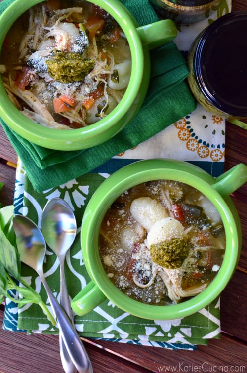 Top view of two green crocks with chicken soup and spoons.