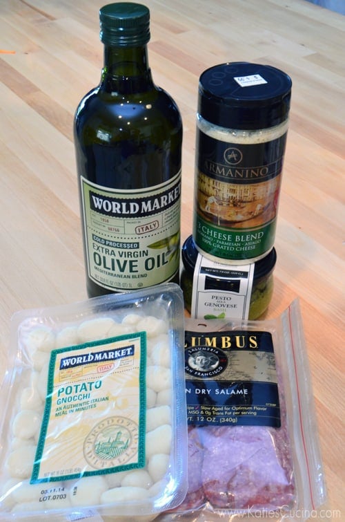 Ingredients on wood countertop; olive oil, cheese, pesto, gnocchi, and salame.