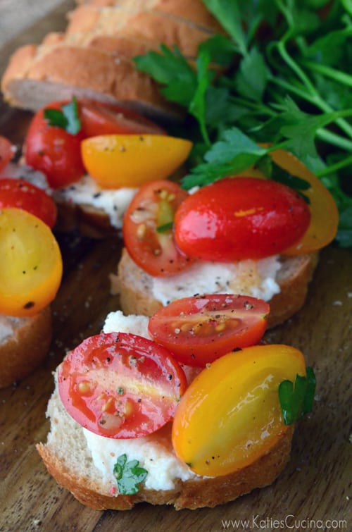 Four slices of baguette topped with ricotta and grape tomatoes.