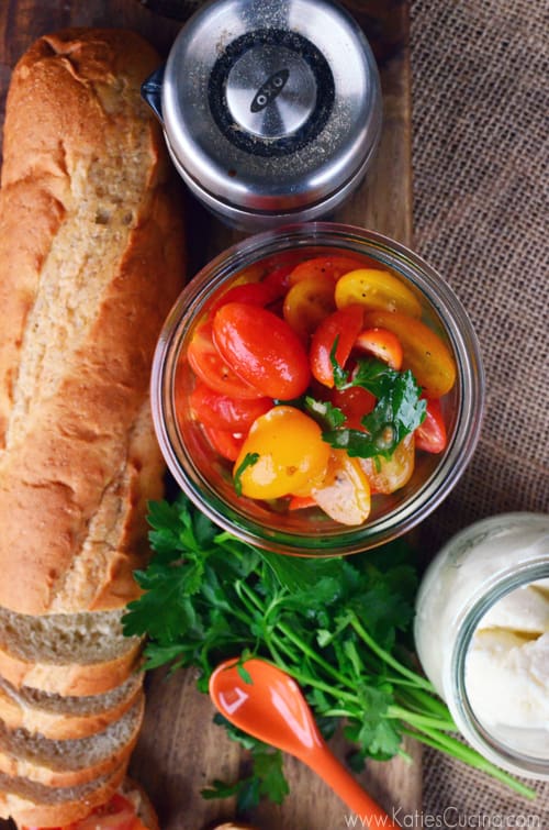 Top view of a jar of sliced grape tomatoes with baguette next to it.