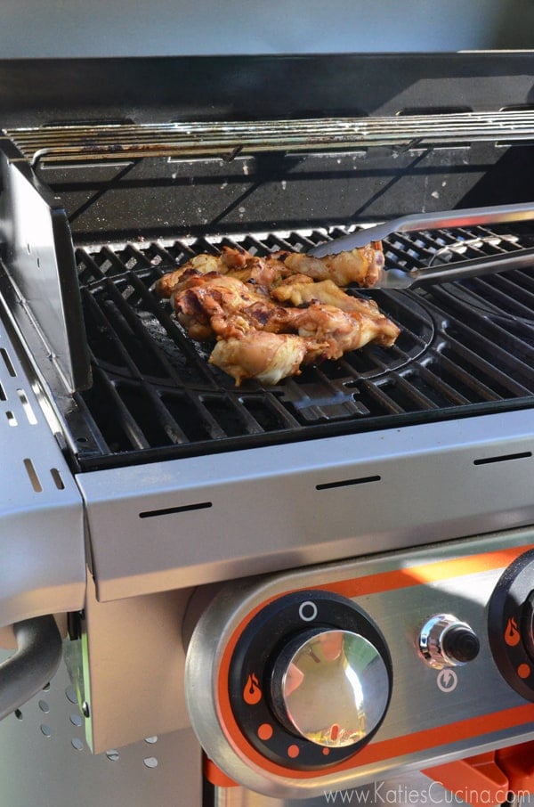 Stainless steal grill with lid open and a ton flipping chicken wings. 