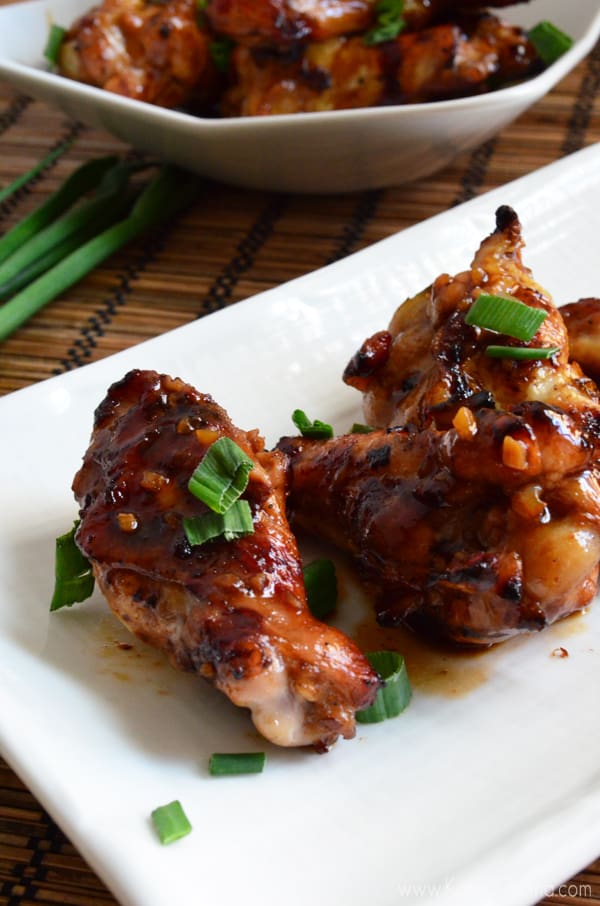 White platter with a few chicken drums in brown sauce topped with green onions.