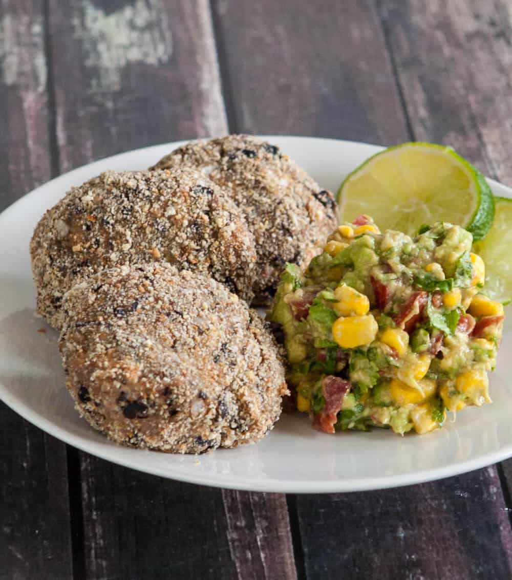 White plate with three breaded croquettes with lime slices and avocado, tomato, corn salad.