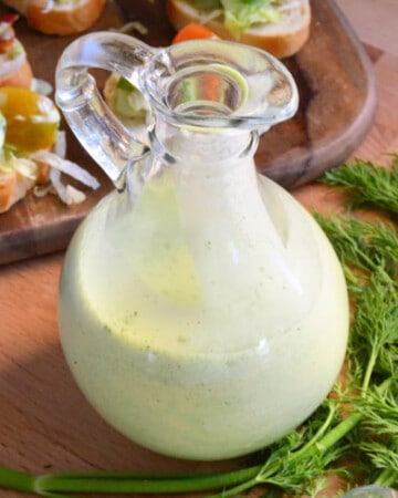 Glass salad dressing with green dressing inside.