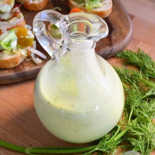 Glass salad dressing with green dressing inside.