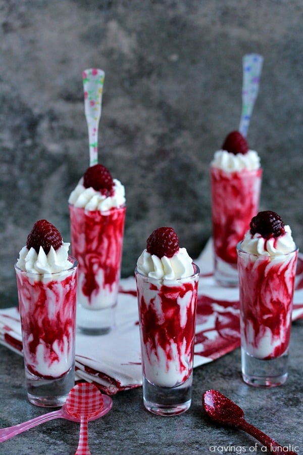 Five skinny tall shot glasses with raspberry sauce and whipped cream. 
