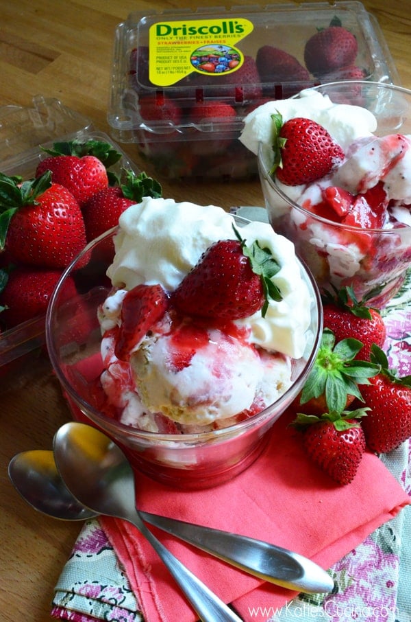 Two strawberry sundaes in glass bowls with fresh strawberries and whipped cream.