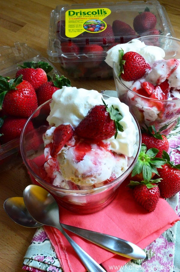 Two strawberry sundaes in glass bowls with fresh strawberries and whipped cream.