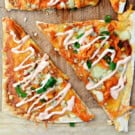 Slices of buffalo chicken flatbread with green onions on a wood cutting board.