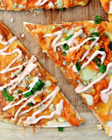 Slices of buffalo chicken flatbread with green onions on a wood cutting board.