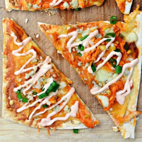 Slices of buffalo chicken flatbread with green onions on a wood cutting board.
