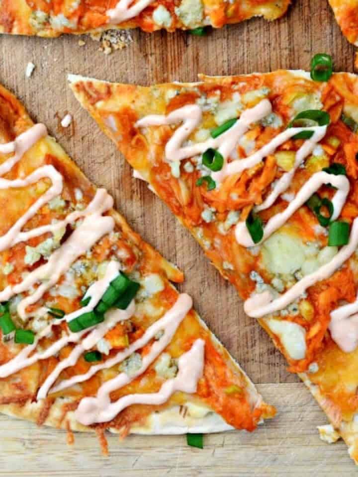 Slices of buffalo chicken flatbread with green onions on a wood cutting board.