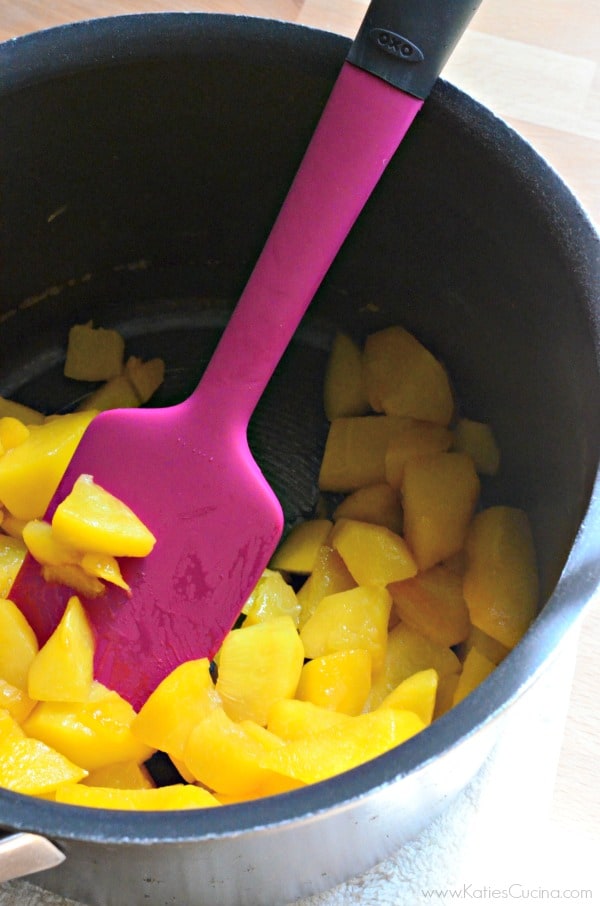 Diced peaches in a black sauce pan with a pink spatula mixing. 