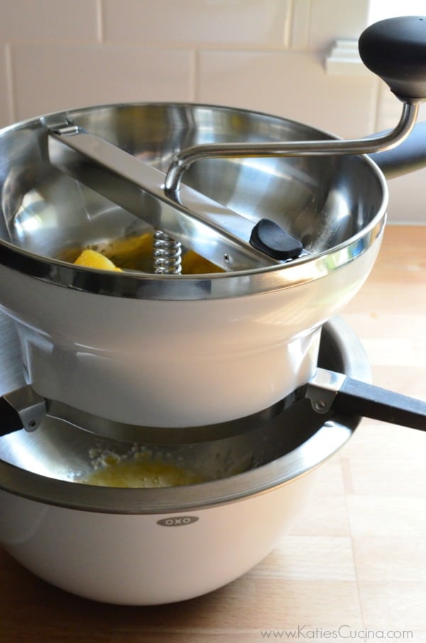 White food mill on top of a white bowl on a wood counter. 