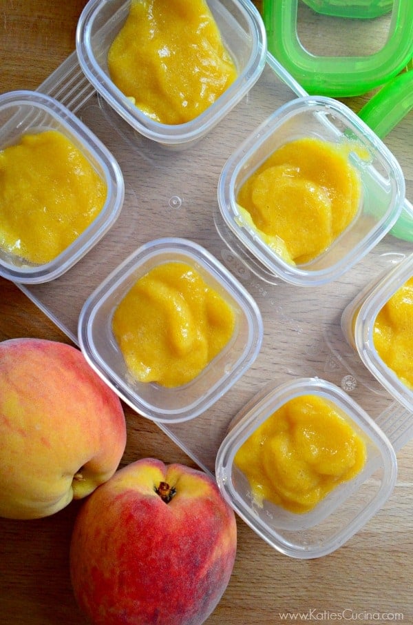 Top view of peach puree in square storage containers on wood countertop with peaches. 