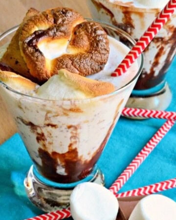 Glass filled with a milkshake with a toasted marshmallow and red and white straw.