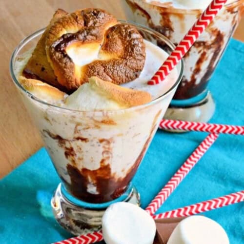 Glass filled with a milkshake with a toasted marshmallow and red and white straw.