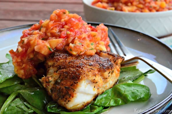 White circle plate with a bed of spinach and blackened fish on top with salsa.