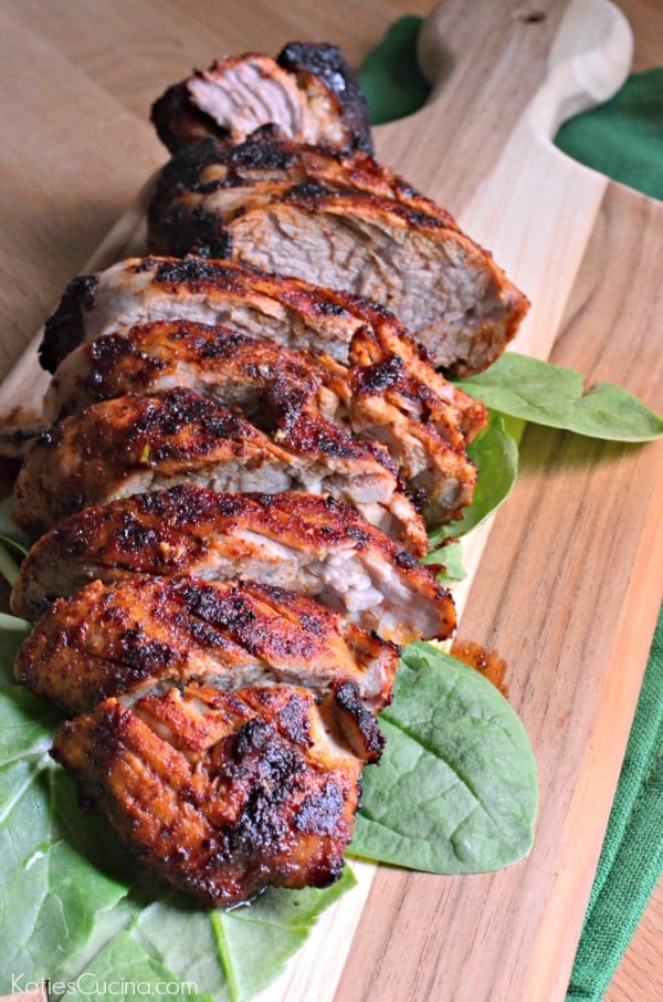Wood cutting board with spinach leaves and slices of brown pork tenderloin.