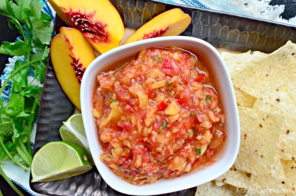 Top view of a square bowl of peach salsa with chips, fresh slices of lime and peaches with chips.