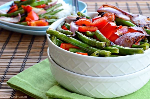 Two white bowls stacked filled with grilled green beans, red bell pepper, and red onions.