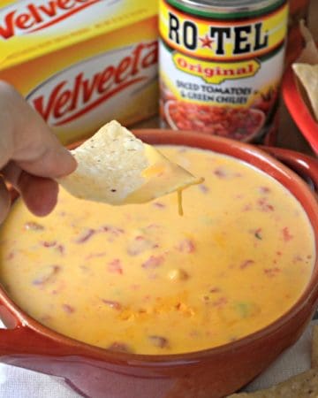 Female hand holding a tortilla chip over a bowl of queso dip.