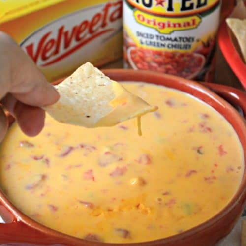 Female hand holding a tortilla chip over a bowl of queso dip.