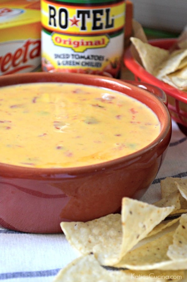 Close up of a red bowl filled with queso dip with chips in front of the bowl.