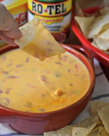 Female hand holding a chip covered in queso dip over a bowl with recipe title text on imaage for Pinterest.