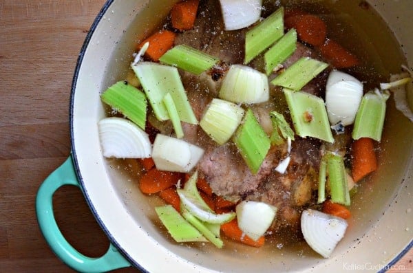 White pot with green handle filled with beef, carrots, onions, and celery.