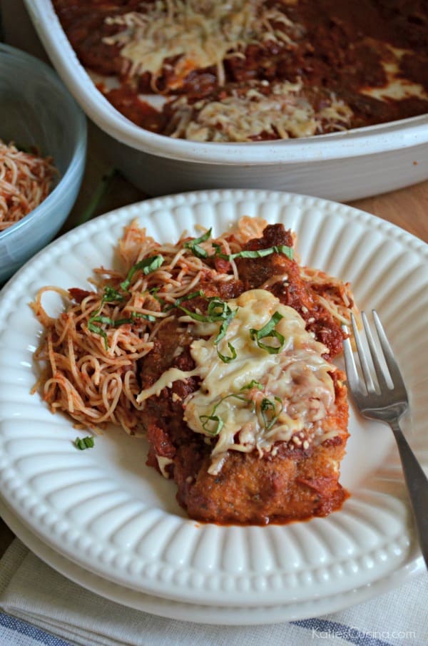 Two plates stacked with a piece of fried chicken parmesan and pasta with fork on plate.