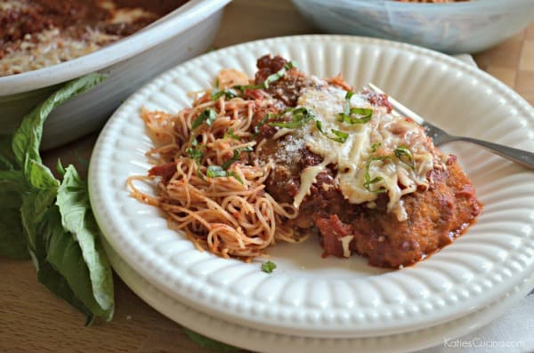 Two white plates stacked with a pile of pasta with chicken parmesan topped with fresh basil.