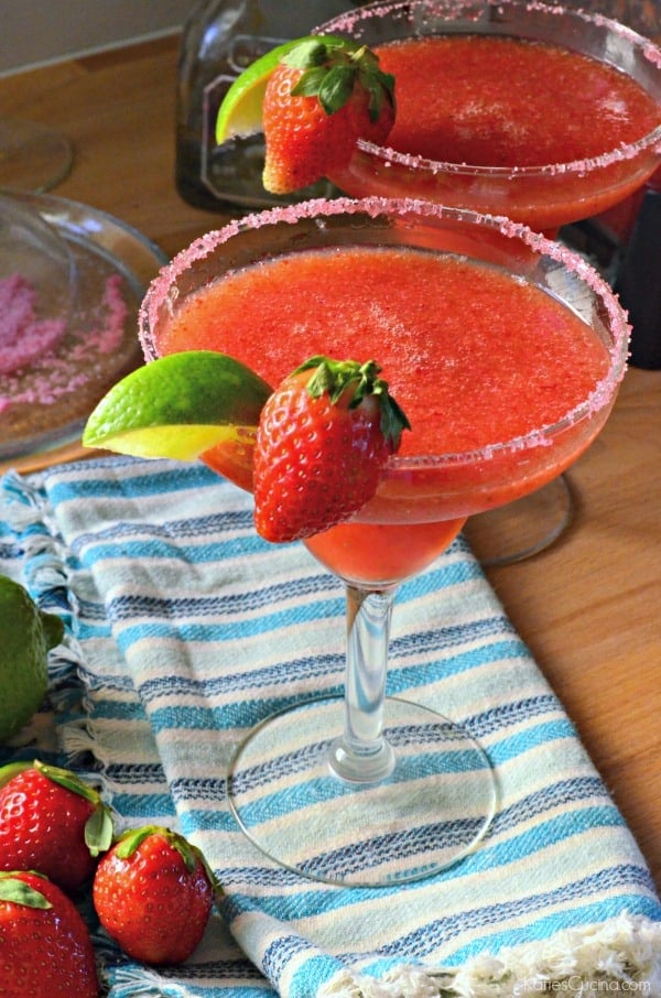 Two Frozen Strawberry Margaritas with sugar on rim with lime and fresh strawberry on glass.