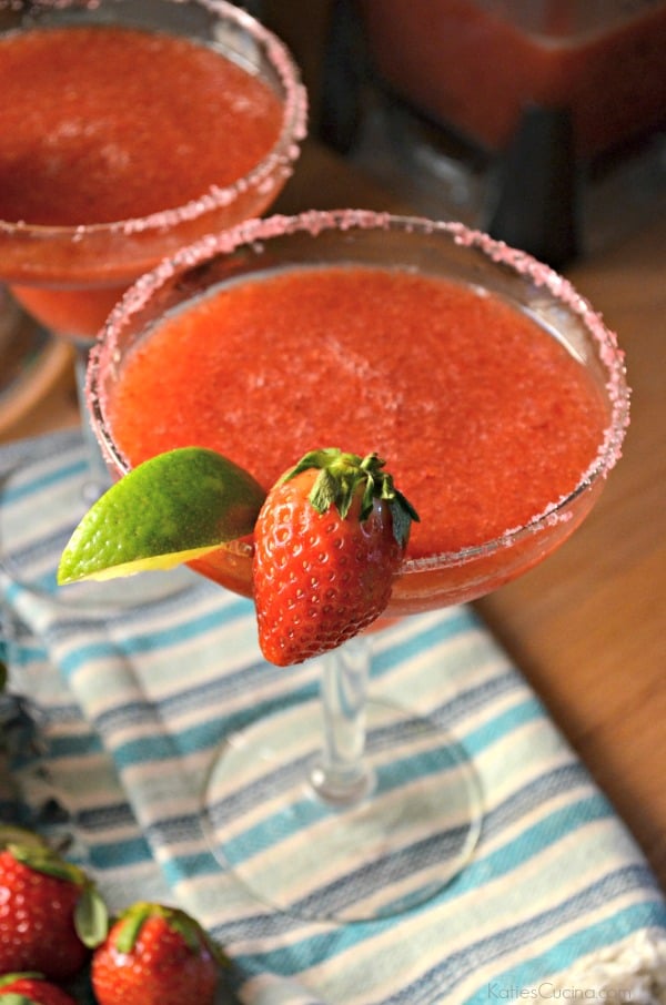 Close up of a strawberry margarita on a wood counter with a blue striped cloth.