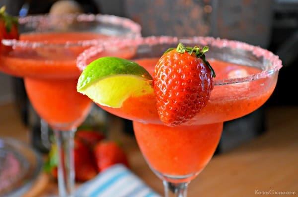 Close up of a horizontal photo of two Frozen Strawberry Margaritas with limes and strawberry garnish.