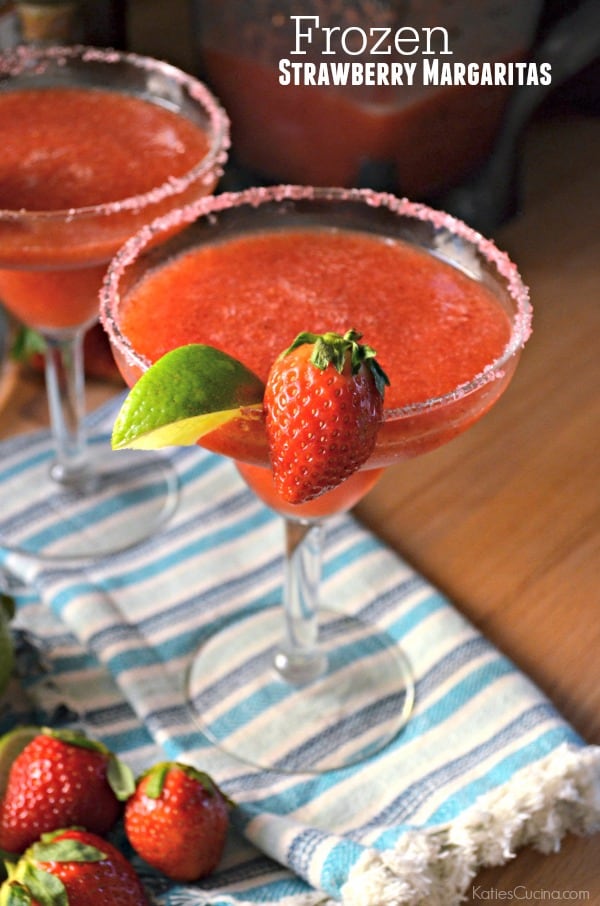 Two frozen strawberry margaritas on a blue striped cloth with text on image for Pinterest.