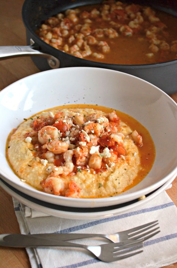 Two white bowls stacked with shrimp and grits and two forks in front of the bowls.