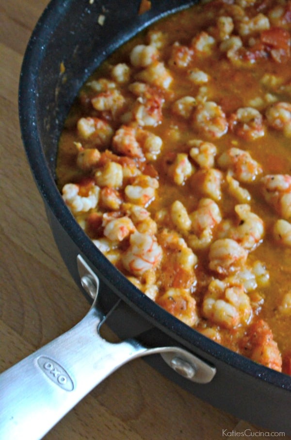 Large black skillet of rock shrimp in a red sauce on top of a wood countertop.